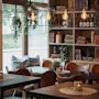 A warm and inviting cafe or lounge area with comfortable seating, soft lighting from candles and hanging bulbs, and a bookshelf.
