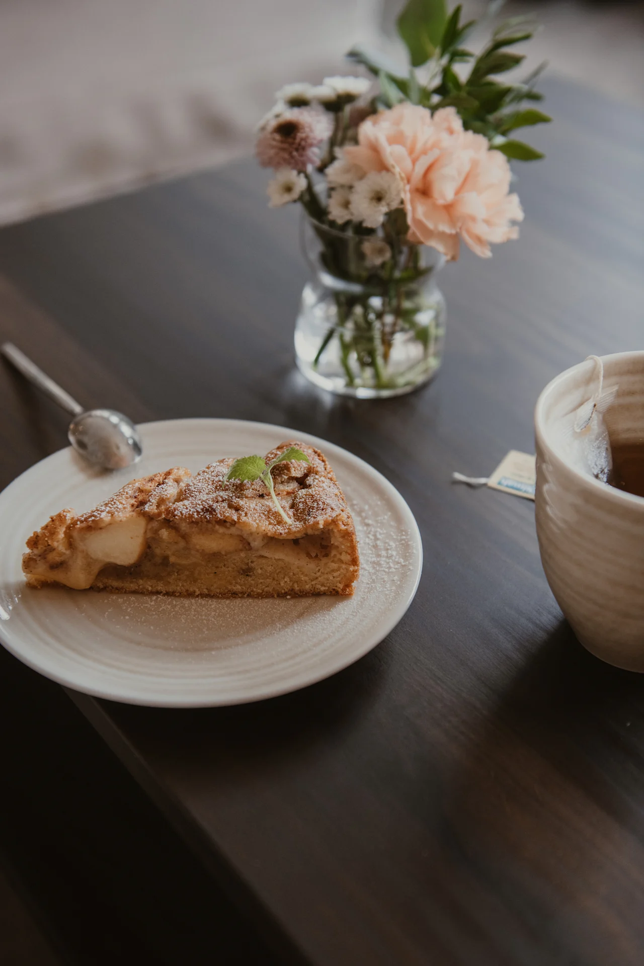 A delightful moment with a slice of cake and a warm cup of tea, accompanied by fresh flowers on a dark table.