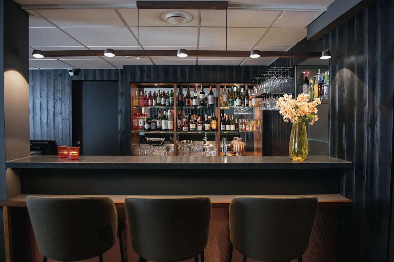 Et koselig og innbydende barområde, klart for gjester å nyte en drink, med et utvalg av drikkevarer og komfortable sitteplasser.