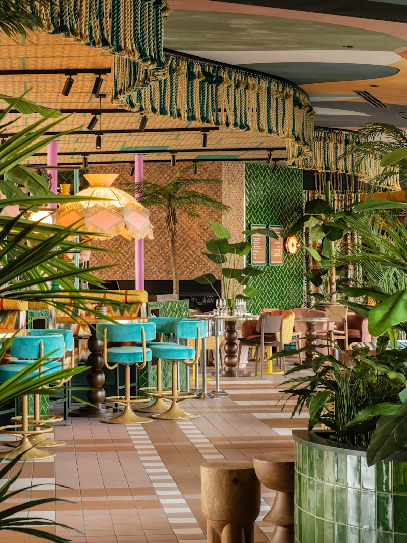 Vehreä kasvivyöhykkeet täyttävät ravintolan, jossa on värikkäitä istuimia ja riippuvia kankaita. Vihreät laatat, eloisat huonekalut ja trooppiset kasvit luovat värikkään, kutsuvan tunnelman.