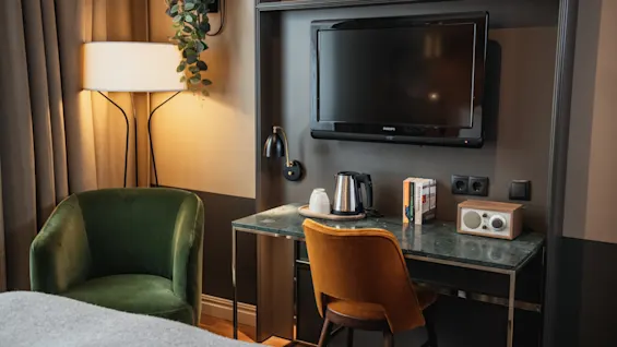 Et velindrettet hotelværelse med et funktionelt skrivebordsområde med fjernsyn, elkedel og radio, suppleret med indbydende lænestole.