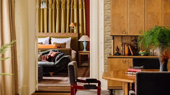 Et rom i vintagestil med elegant møblement som ser inn i et koselig soverom med varmt lys.