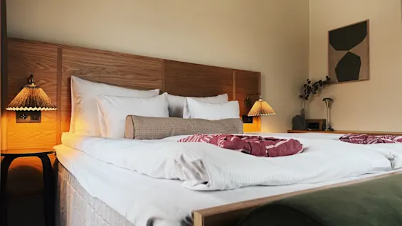 Ett mysigt hotellsovrum med en stor säng, vita lakan och varm belysning från sänglampor. Ett inbjudande utrymme för vila.