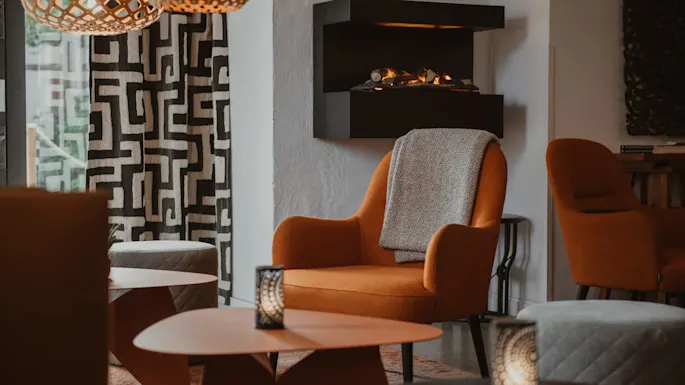 Et hyggeligt loungeområde med orange lænestole, en moderne pejs og stilfuld belysning, der skaber en varm og indbydende atmosfære.