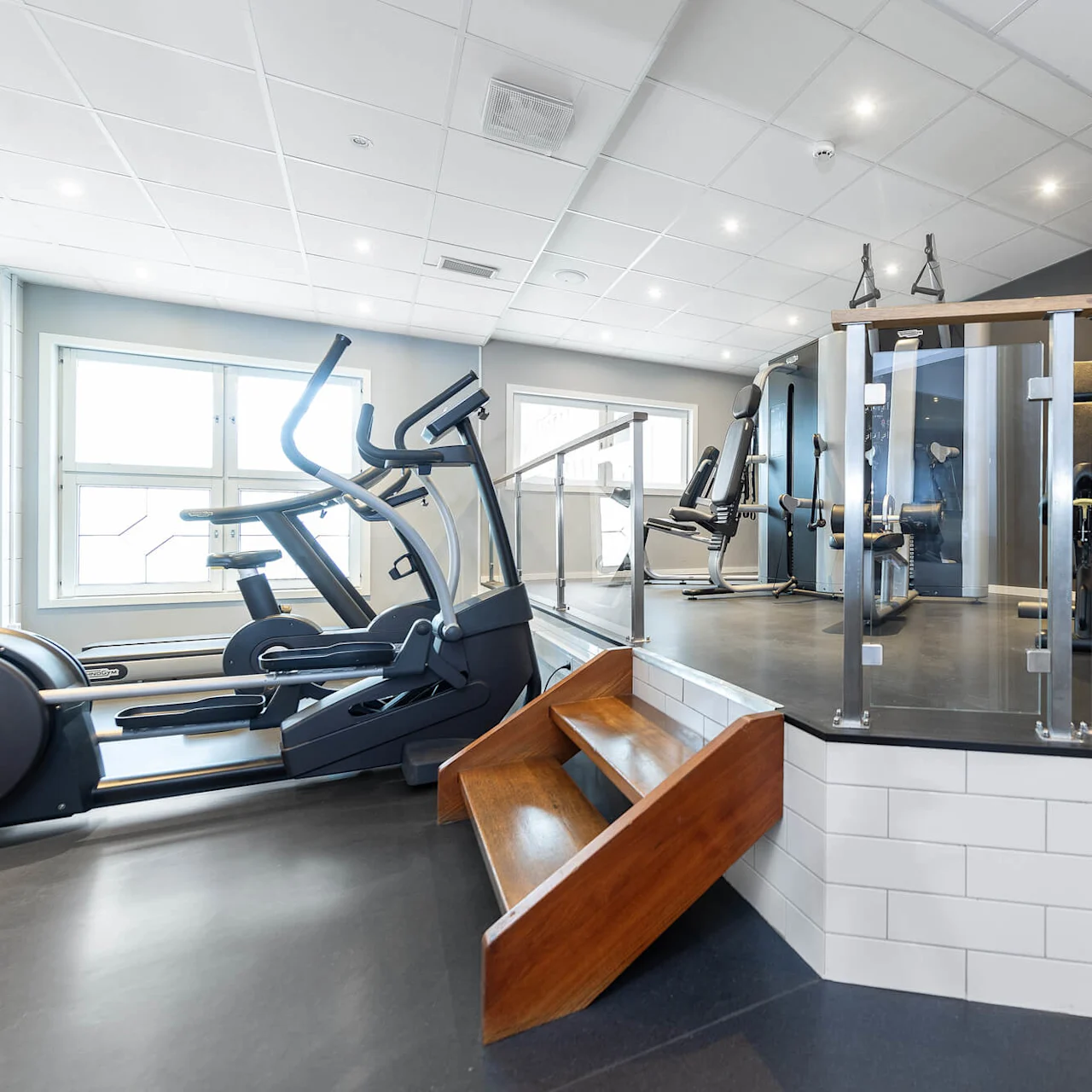 Exercise equipment in a well-lit gym with treadmills, weights, and mirrors.