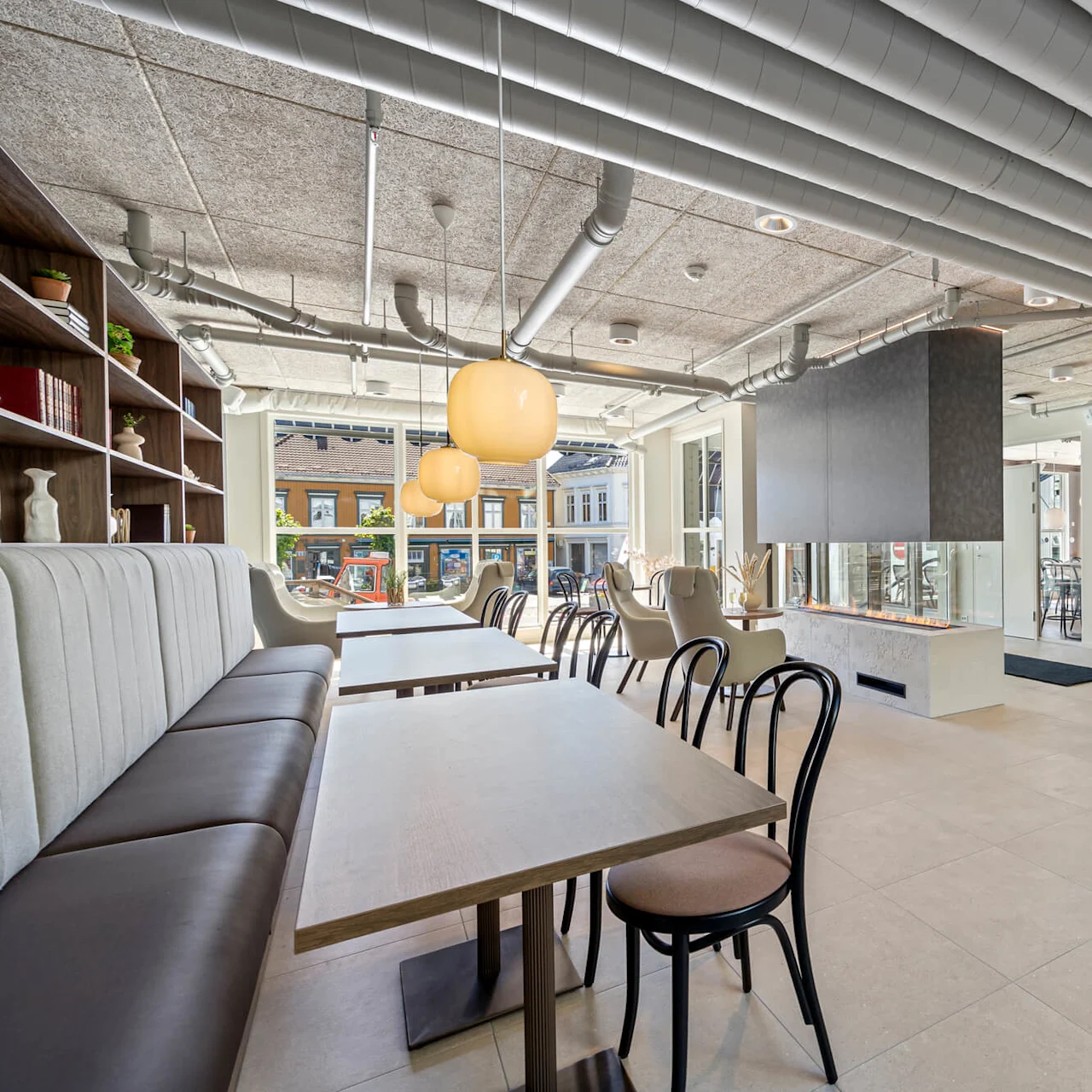 A modern, well-lit interior with dining tables, a sofa, decorative lighting, and artwork, visible through large street-facing windows.