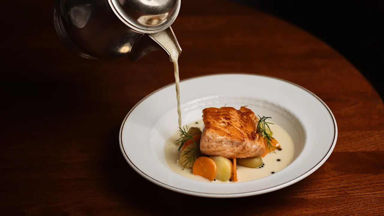 Tyylikäs lohi- ja kasvisruoka saa viimeisen silauksen, kun kermainen kastike kaadetaan hopeakannusta.