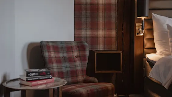 En hyggelig læsekrog i et værelse med en ternet lænestol, et lille bord med bøger og en seng med læselampe.