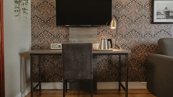 A welcoming hotel room at Home Hotel Grand, Helsingborg, with a patterned wall, a desk, TV, and amenities for comfort.