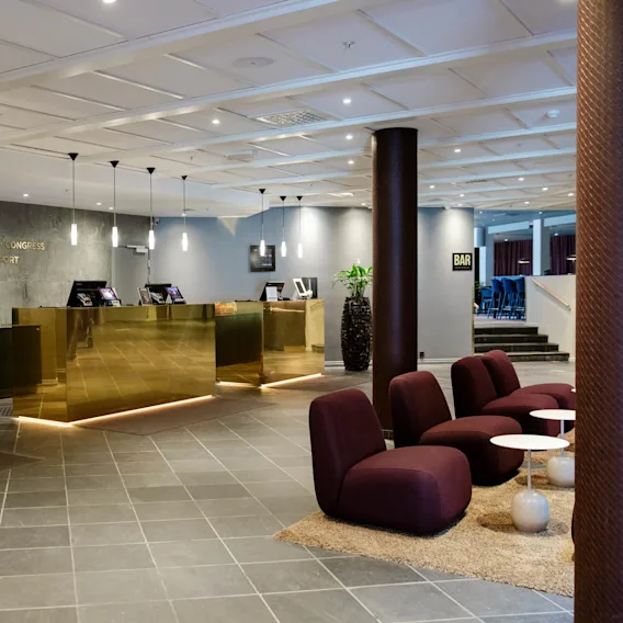 Reception desk with gold accents stands in a modern hotel lobby, surrounded by purple chairs and small tables. Text reads: "Clarion Hotel & Congress Oslo Airport."