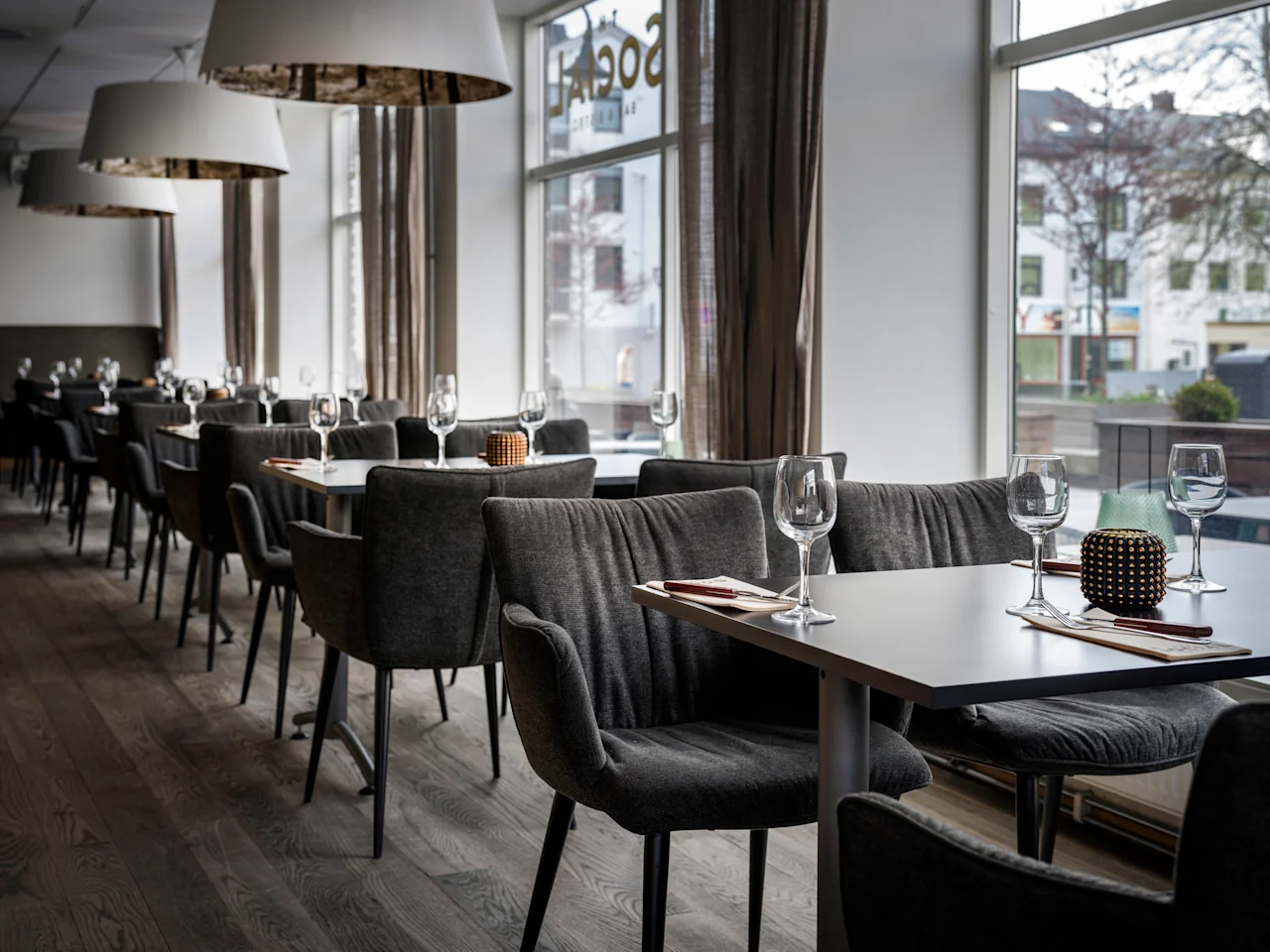 A spacious dining area with many tables set for guests, featuring large windows and modern lighting.