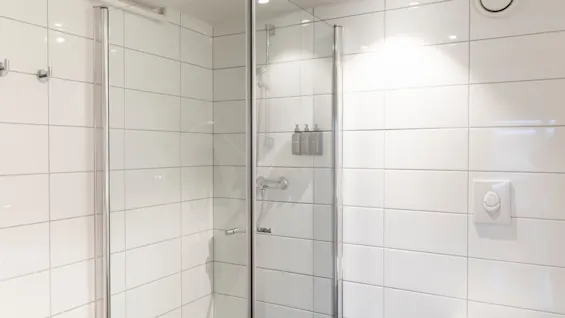 Et lyst, moderne baderom med en dusj i glass, hvite flislagte vegger, et toalett og rene armaturer.