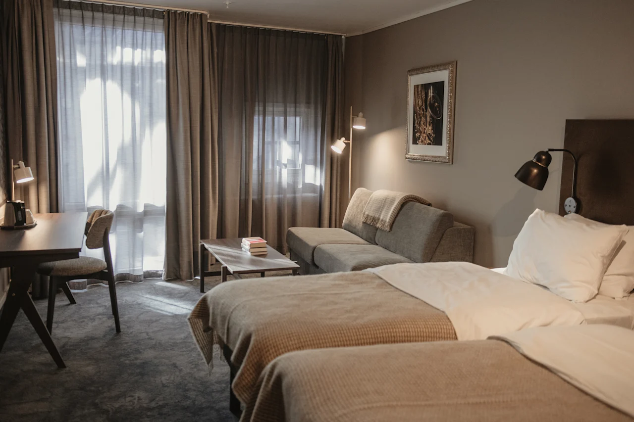 Et koselig hotellrom med to senger, en sofa, et skrivebord og varm belysning, perfekt for avslapning eller arbeid.