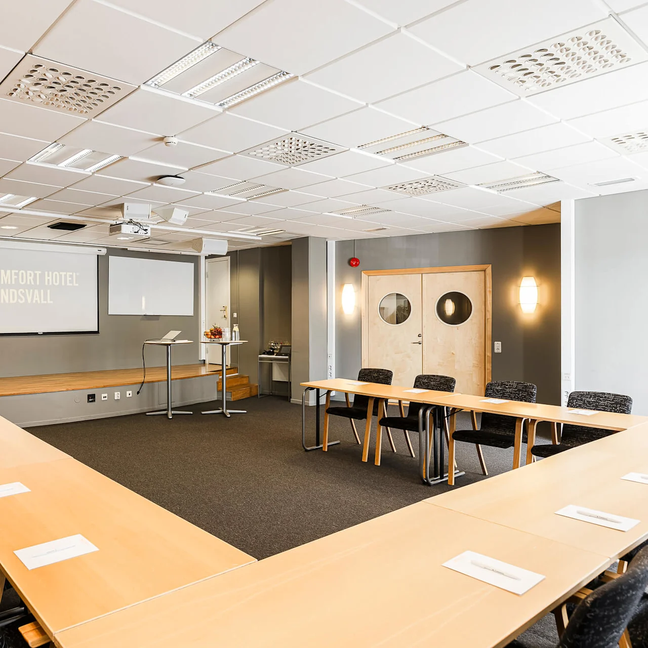 Ett tomt konferensrum med bord, stolar och presentationsteknik. "COMFORT HOTEL SUNDSVALL" projiceras på skärmen.