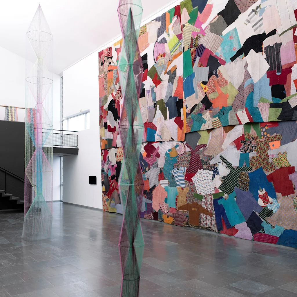 A vibrant art installation at Lunds Konsthall in Lund featuring a large patchwork textile wall and delicate woven sculptures.
