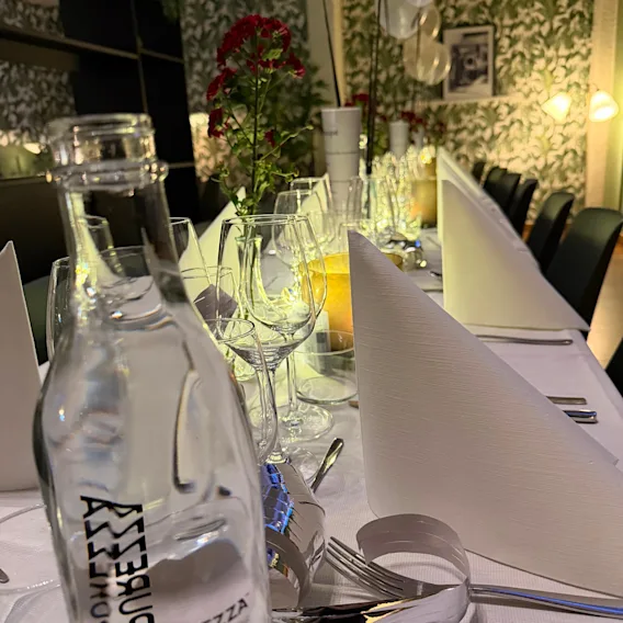 Ett långt dukat festbord med vita servetter, vinglas, blommor och ballonger i en stämningsfull restaurang.
