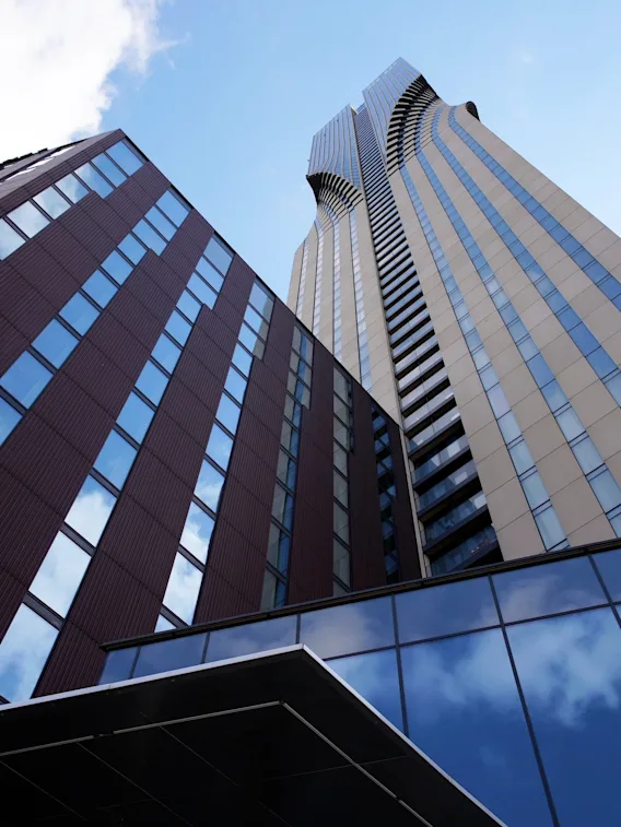 En lågvinkelvy av två moderna höghus mot en blå himmel med moln, som visar arkitektonisk design.