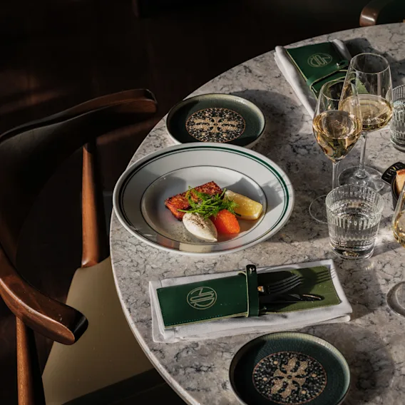 Kauniisti katettu marmoripöytä, jossa on gourmet-annos, viinilaseja ja tyylikäs kattaus lämpimässä auringonvalossa.
