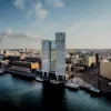 Aerial view of a modern city skyline with a tall building by the waterfront, boats docked, and a partly cloudy sky. Text: HELSINKI