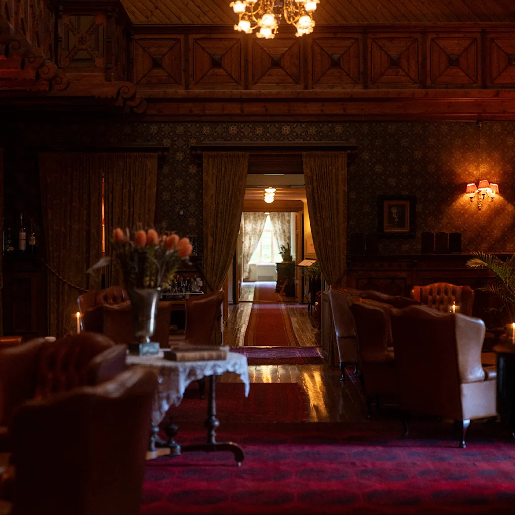 Cozy and elegant interior of Dalen Hotel, featuring warm lighting, plush seating, and a vase of flowers. A glimpse through the curtains reveals a sunlit area in the distance, creating a welcoming atmosphere.