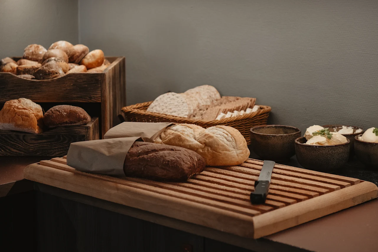 Ett frukostbord med olika färska bröd, inklusive frallor, limpor och tunnbröd, tillsammans med skålar med smör och en kniv.