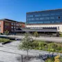 Modern hotel building in bright sunshine with a lush green park and paved walkway under a clear blue sky