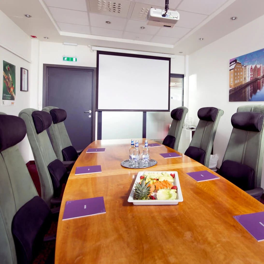 A conference room with a long table, chairs around it, and a blank projector screen, suggesting a business setting.