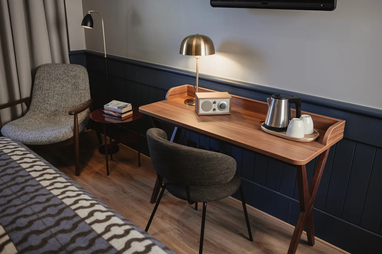 Ett mysigt hotellrum med ett träskrivbord med vattenkokare, koppar och en radio, tillsammans med en bekväm fåtölj och säng.