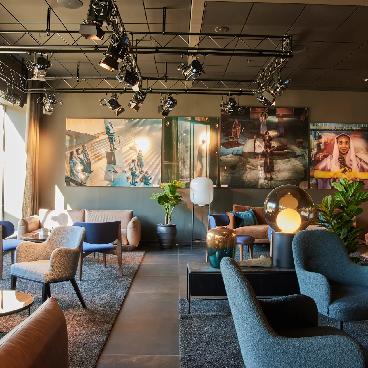 Ett modernt loungeområde har eleganta stolar och bord arrangerade på en mattbelagd golvyta under takspotlights. Stora fönster släpper in naturligt ljus och inramad konst dekorerar väggarna.