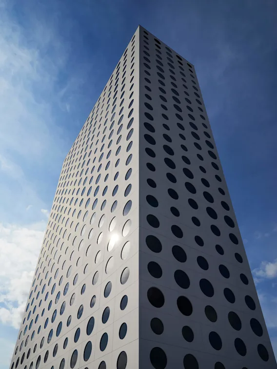 En moderne høy bygning med mange runde vinduer strekker seg oppover mot en blå himmel med spredte skyer. Sollys reflekteres fra fasaden, noe som skaper et slående mønster.