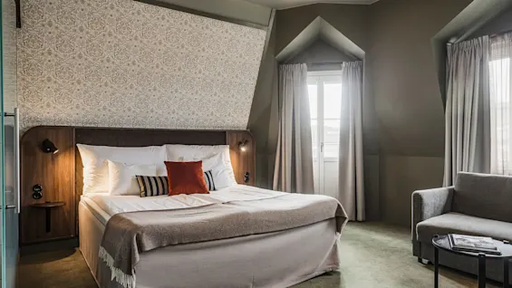 En snyggt bäddad säng centralt placerad i ett välbelyst hotellrum med eleganta dekorationer och bekväma möbler.