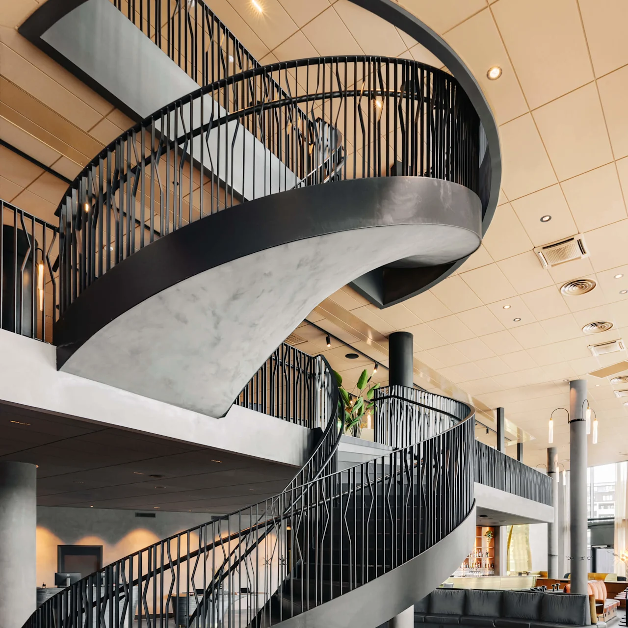 En modern spiraltrappa reser sig elegant, inramad av snygga svarta räcken, i ett rymligt och modernt öppet interiör med dämpad belysning och rundad sittplats.