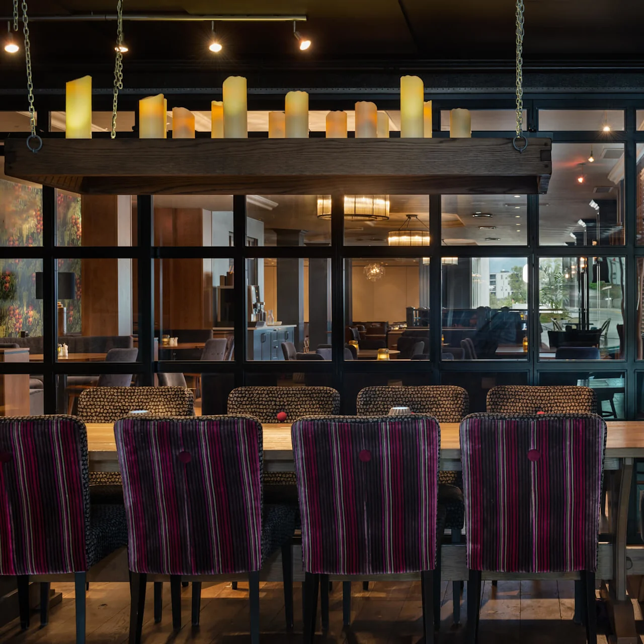 Ett långt matbord med randiga stolar i en elegant restaurang. Ovanför finns en hylla med tända ljus och mjuk belysning skapar en mysig atmosfär.