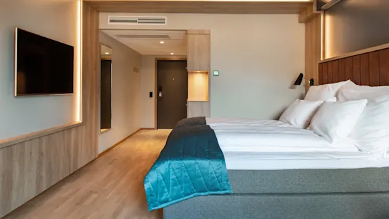 Et moderne hotelværelse med en komfortabel seng, et vægmonteret TV og varm belysning.
