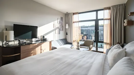 A bright and modern hotel room at Farris Bad in Larvik with a large bed, seating area, and a view of the city.