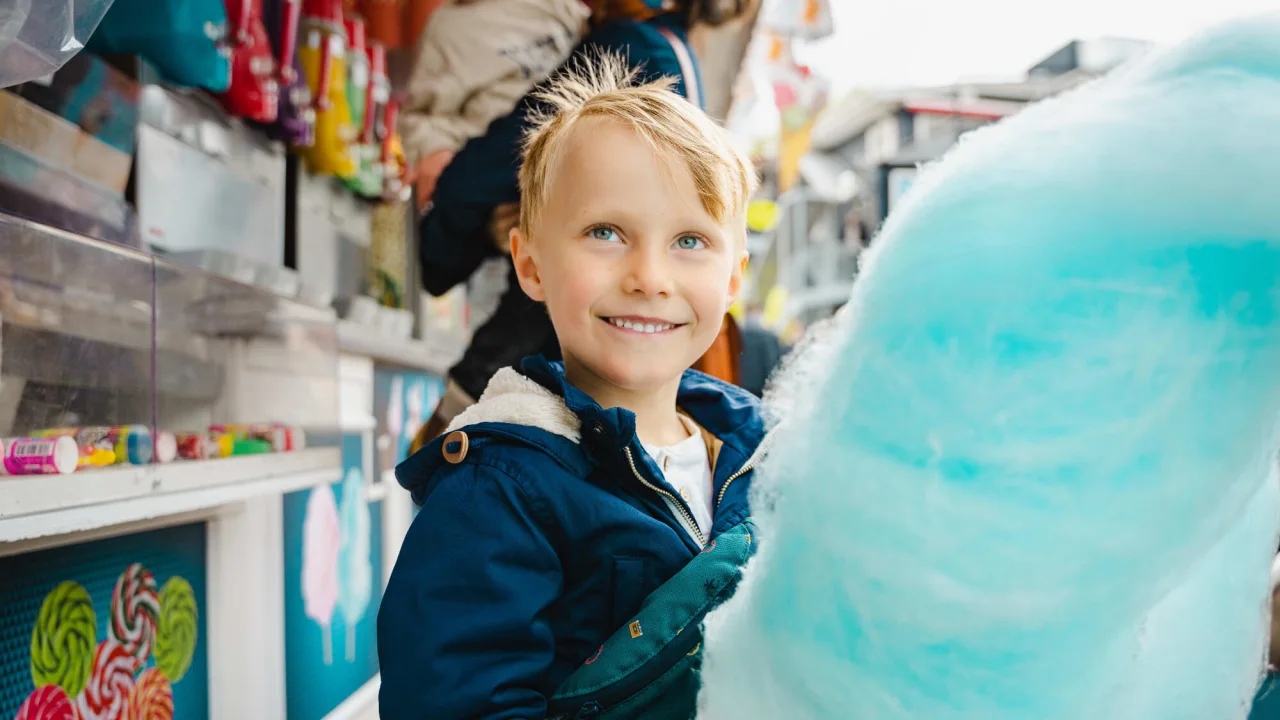 Boy eating blue cotton candy at amusement park Bakken in Copenhagen.