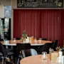 Runde bord med glass og bestikkholdere er arrangert i en restaurant. En tavle ovenfor sier: "Wine, I MAKE wine disappear, What's Your SUPERPOWER, In vino veritas," med vinrelaterte tegninger.
