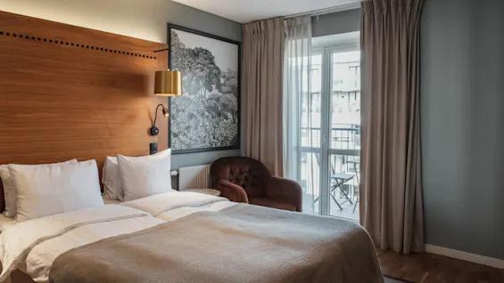 Et komfortabelt hotelværelse med en stor seng, en hyggelig lænestol og en balkon med udendørs siddepladser, perfekt til afslapning.