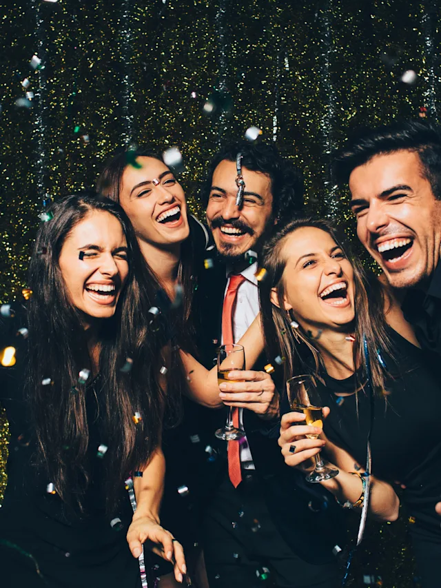 A joyful group celebrating, with laughter and drinks amidst falling confetti.