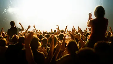 En livlig publik på en konsert eller ett evenemang, med många händer uppsträckta i spänning mot starka scenljus.