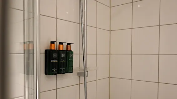Flaskor monterade på en duschvägg innehåller balsam, schampo och duschtvål i ett kaklat badrum. Text på flaskorna: ”conditioner,” ”shampoo,” ”shower gel,” ”RITUALS,” ”Ritual of Jing.”