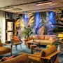 Komfortabel siddeområde med træstole og sofaer, med tropisk-inspireret tapet omgivet af frodige grønne planter, der skaber en hyggelig og livlig atmosfære.