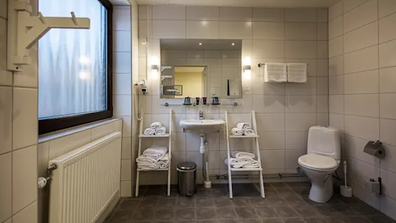 A tidy bathroom with tiled walls and floor, showcasing a sink, toilet, and shelves with towels, in a well-lit, clean setting.
