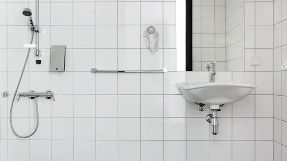 A white, wall-mounted bathroom sink with a faucet and a shower head on tiled walls.