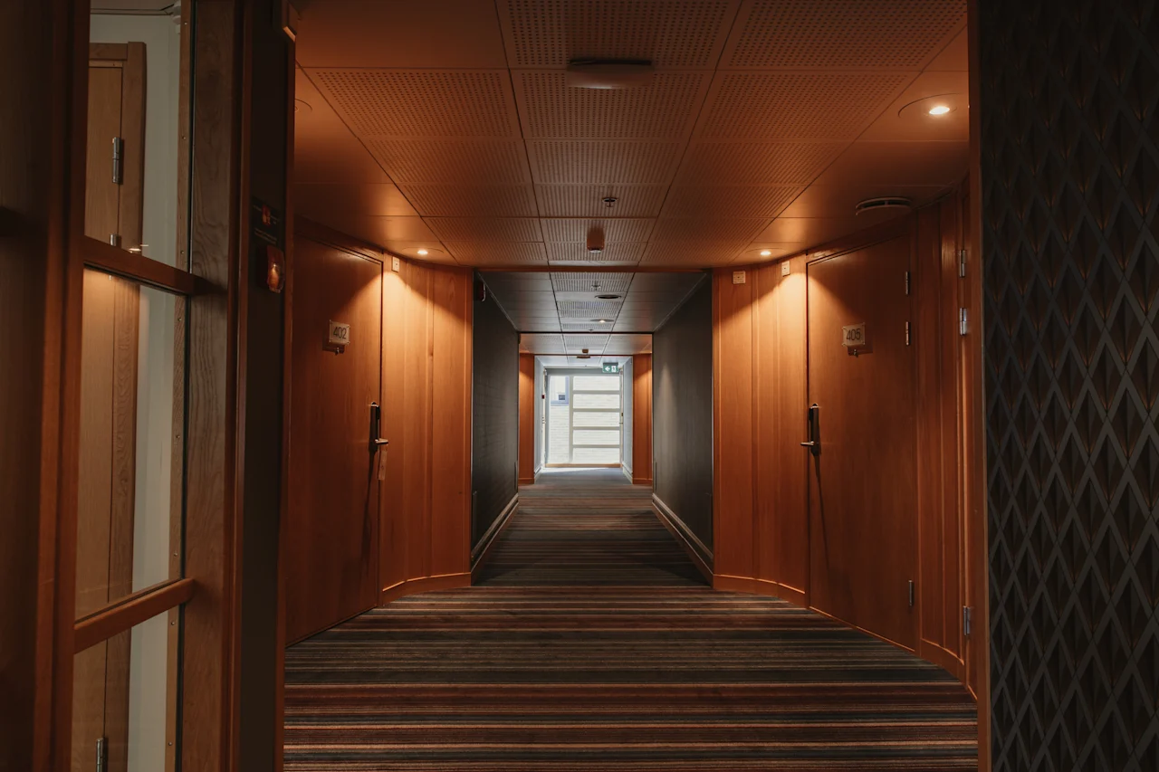A warm, inviting hotel hallway at Home Hotel Uppsala with wooden doors and a striped carpet leading to a bright area.
