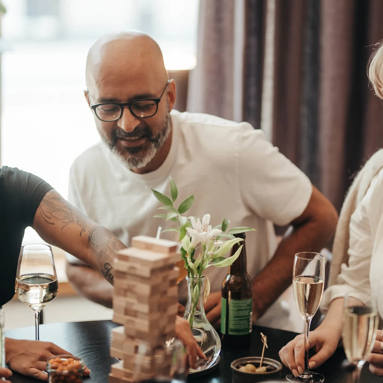A group of people playing Jenga and socializing around a table with drinks and snacks in a cozy indoor setting.