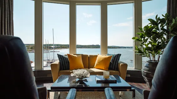 Et hyggeligt loungeområde med sofa og lænestole, med panoramaudsigt over en bugt med både gennem store vinduer.