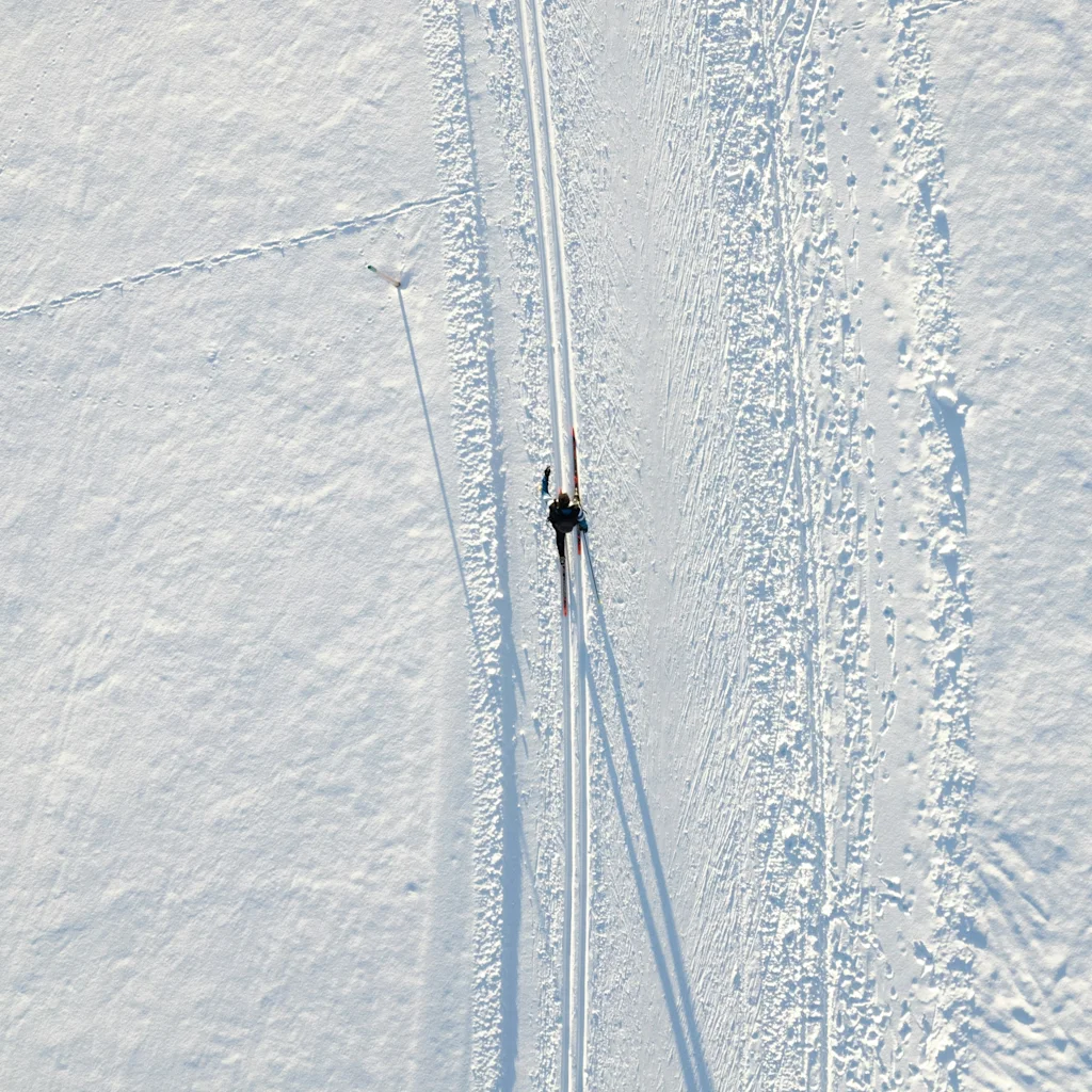 Två personer åker längdskidor på ett preparerat spår i ett vidsträckt snölandskap under en klar himmel.