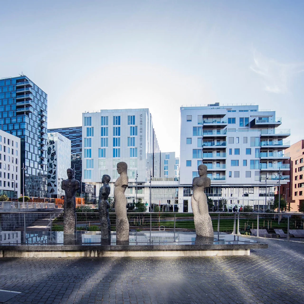 Statues standing silently on a reflective surface amid modern buildings and clear sky in an urban environment.