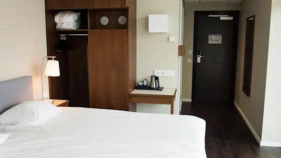 Siisti ja toimiva hotellihuone, jossa on sänky, vaatekaappi ja pieni pöytä vedenkeittimellä.
